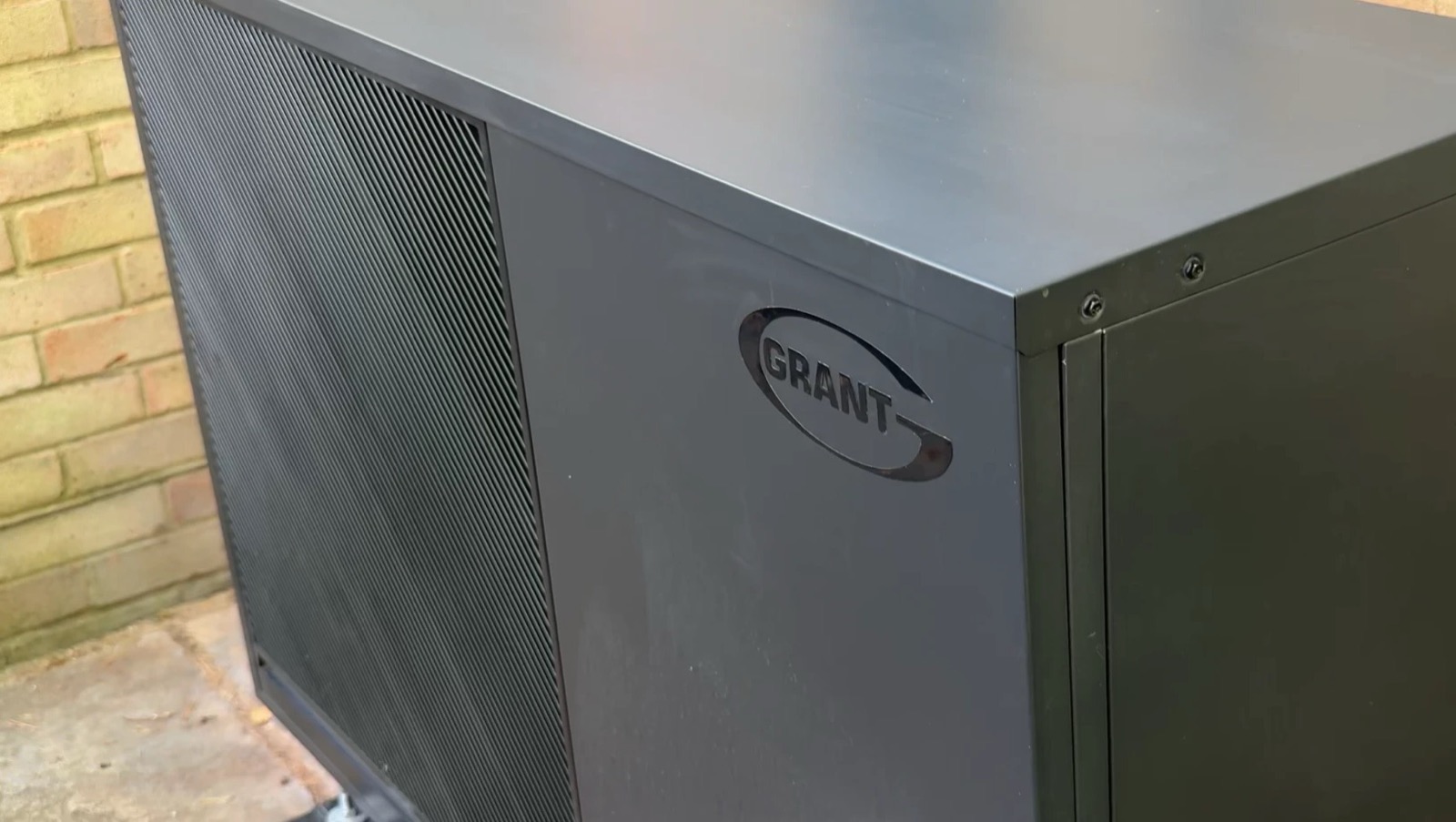 The black Grant Aerona R290 heat pump outside, against the brick wall
