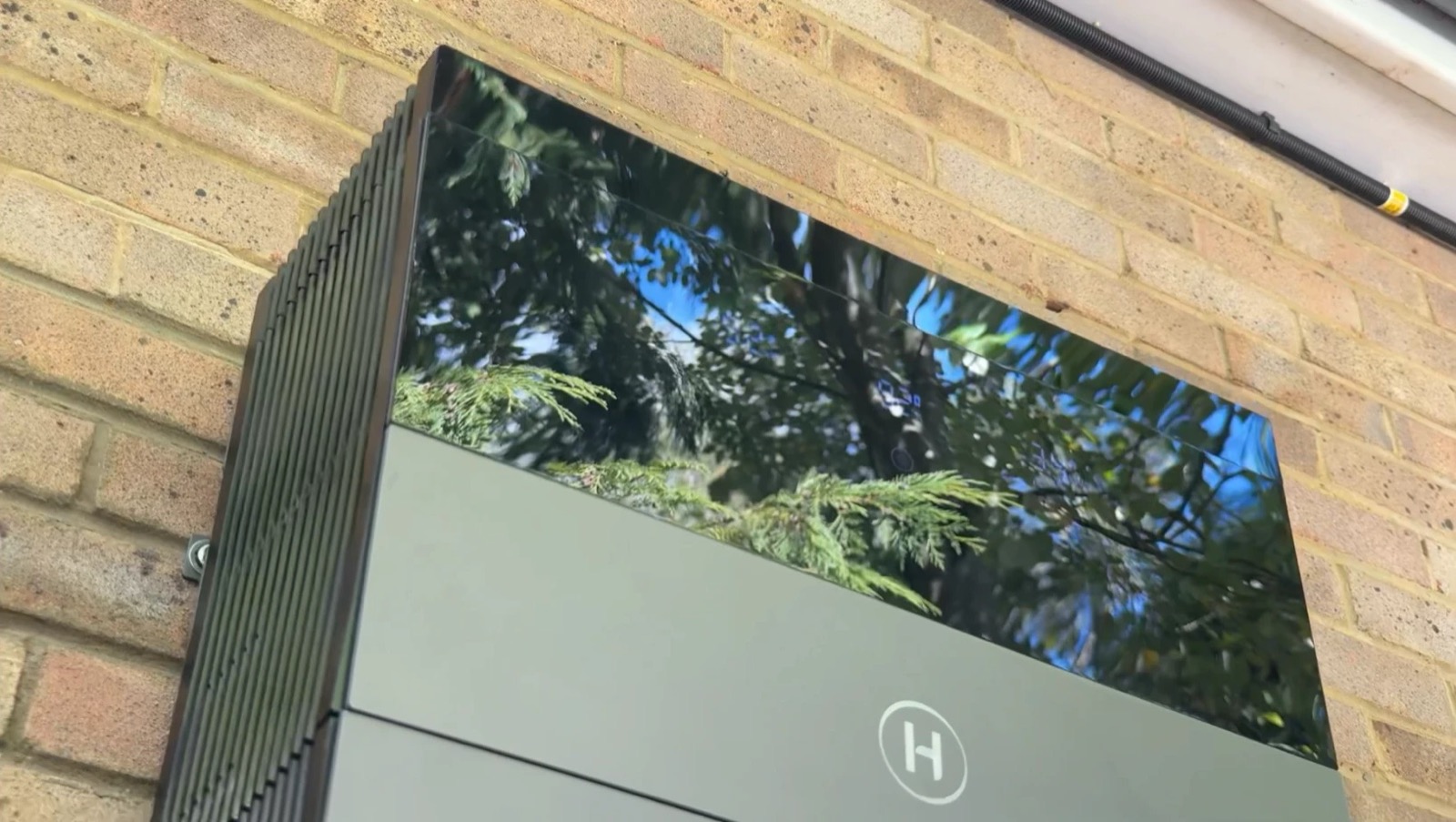 The Hoymiles HiOne battery and controller mounted on the outside wall, its glass top reflecting trees
